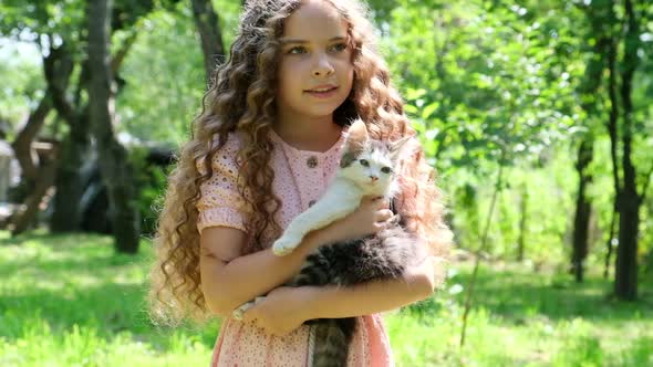 Little Girl with Curly Hair Holding a Little Cat in Her Arms