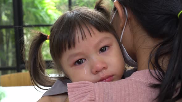 Asian girl is crying in in arms of mom. A mother comforts her crying daughter