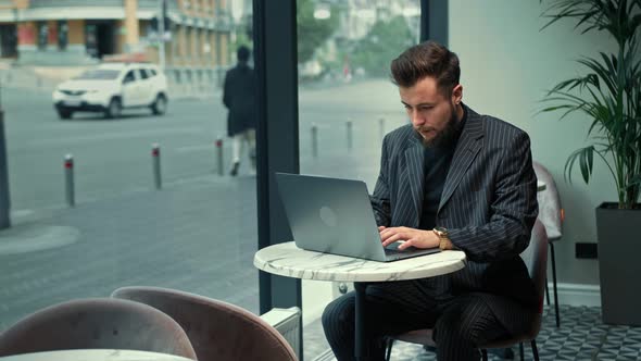 Bearded man is working on laptop in a coffee shop. Freelancer, businessman.