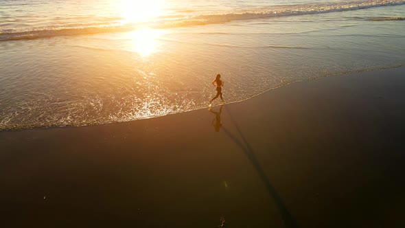 Aerial shot of fit asian woman jogging on the beach at sunset