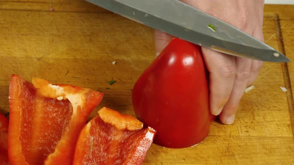 Close-up of a cook cutting red bell peppers on a kitchen board. View from above