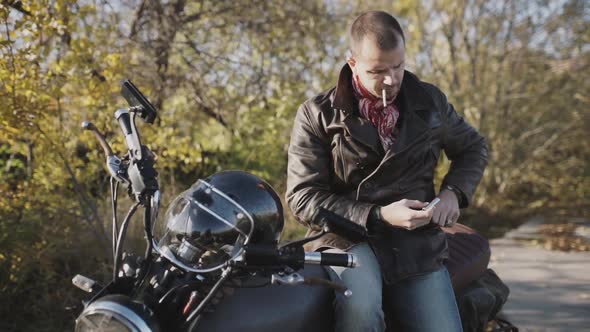 Young Man Motorcyclist Smokes a Cigarette While Sitting on a Motorcycle