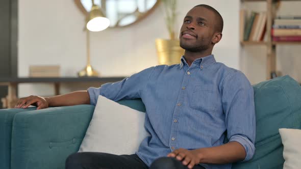 Happy Young African Man Sitting on Sofa Thinking