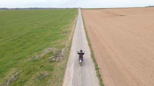 Drone actively tracking an accelerating motorcycle rider along an empty gravel road in the European