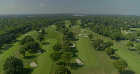 Flying Over a Golf Course with Trees Near a Forest on a Sunny Day