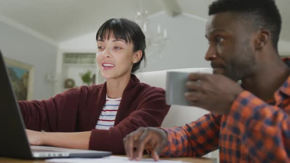 Happy diverse couple sitting at table and working with laptop