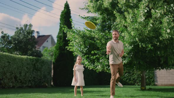 Happy Father and Daughter Playing with Flying Disc on Backyard