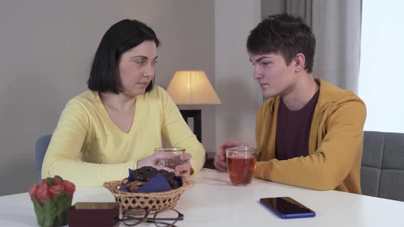 Portrait of Confident Teenage Caucasian Boy Sitting at the Table with Mother and Talking. Adult