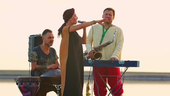 Ethnic Band Is Performing on Stage Near the Sea, Hang Drum, Saxophone, Singing