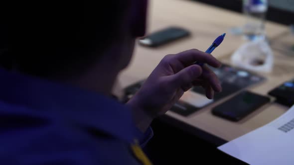 A Man in a Blue Shirt Holds a Pen Against the Background of a Desk
