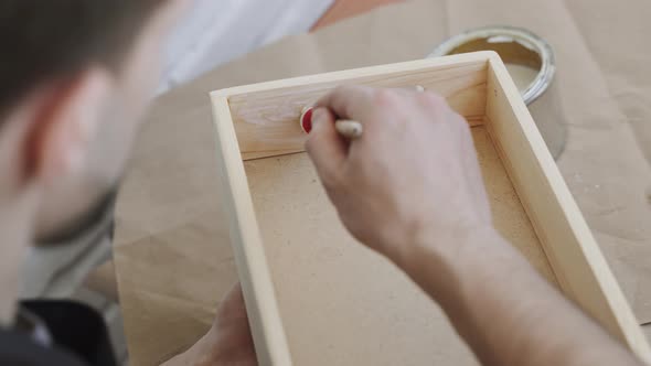 Craftsman Covers Surface of Homemade Wooden Box with a Protective Liquid