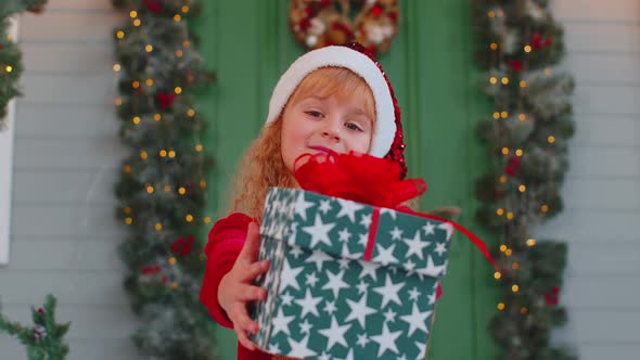 Happy Toddler Child Girl Kid in Red Sweater Gifting One Christmas Present Box Stretches Out Hands