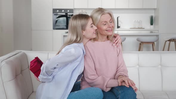 Adult Daughter Presenting Birthday Gift Box To Happy Old Mother Smiling Bonding Embracing Young