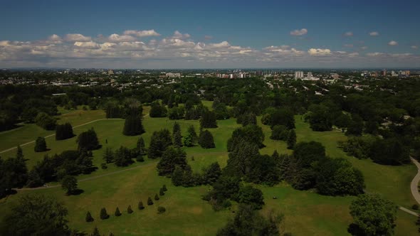 An aerial drone shot over Maisonneuve park in Montreal, blue sky, green trees, tilt down