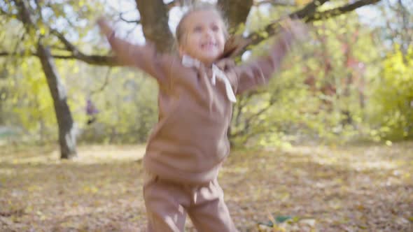 Girl Throws Autumn Yellow Leaves Up and Laughs Kid is Having Fun Playing City Nature Park Outdoors