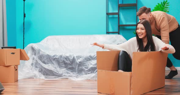 Happy Young Couple Moving Into New Apartment Boyfriend Drives Girlfriend in Cardboard Box She