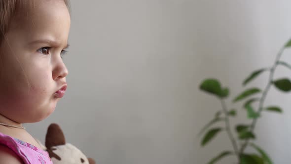 Small Toddler Girl Making Funny Expressive Grimace Face with Soft Toy Bear at Home