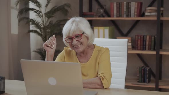 Beautiful Smiling Older Woman Is Using a Laptop Computer for Online Video Call at Home Office. A