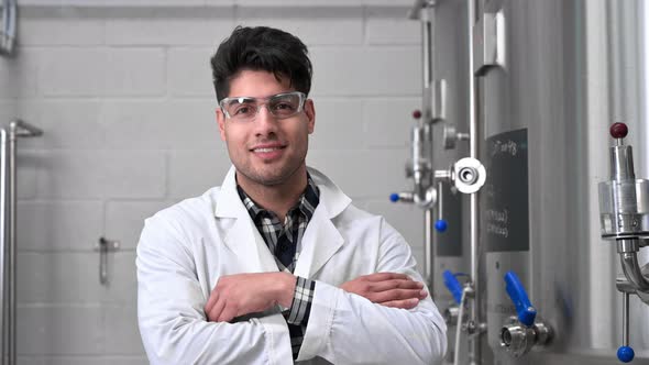 Young Handsome Male Worker in White Lab Coat Smiling and Looking to Camera Standing at Rows of Steel