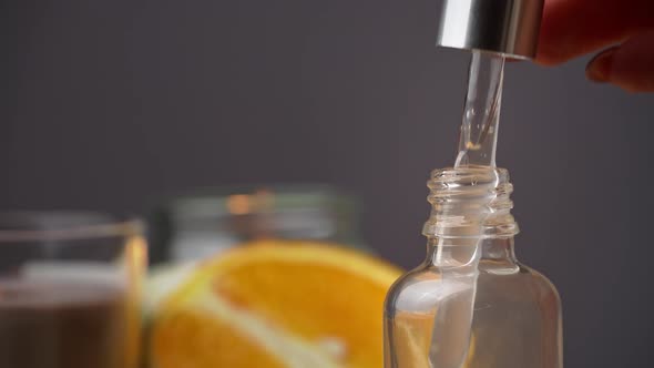 Essential Oil Drips From a Pipette Into a Bottle on the Background of a Candle