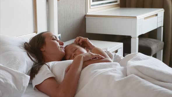 Mother Lying on Bed with Her Sleeping Child at Home