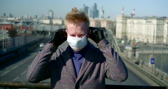 Young Man Is Putting Surgical Mask on Face for Protecting From Coronavirus Standing Outside in City