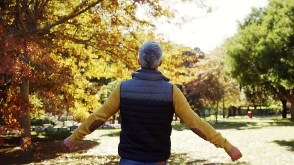 back of man walking outdoors raising hands