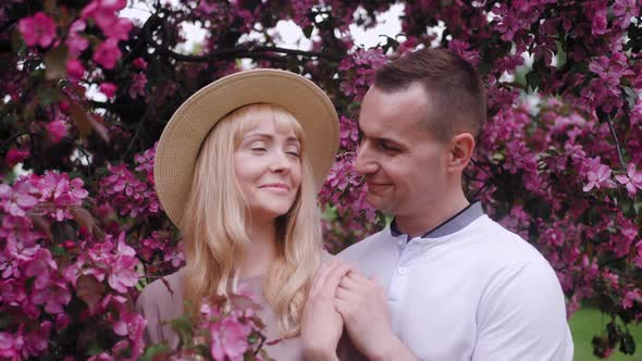 Romantic Beautiful Woman in a Hat Stands with a Man at a Cherry Blossom Tree in the Summer in the