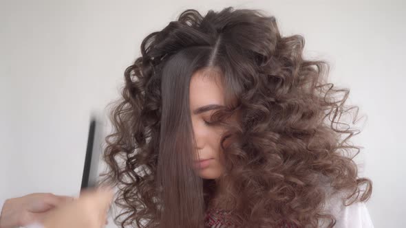 A hair stylist makes a hairstyle for a young beautiful girl with long dark hair