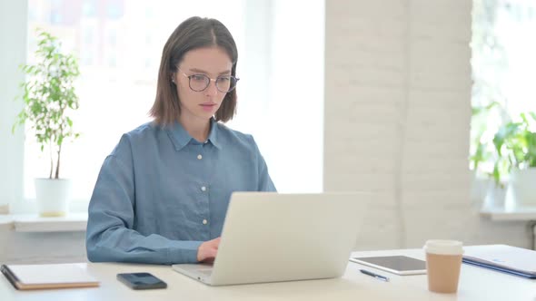 Young Woman Looking at Camera while using Laptop in Office