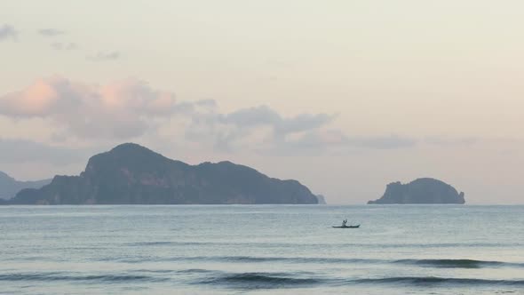 Slow motion shot of paddling man in boat in front of limestone cliffs at dusk seen from beach