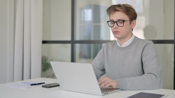 Young Man Shaking Head As No Sign While Using Laptop in Modern Office