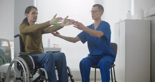 Rehabilitation Doctor Helping Patient in Wheelchair to Workout with Stretch Band