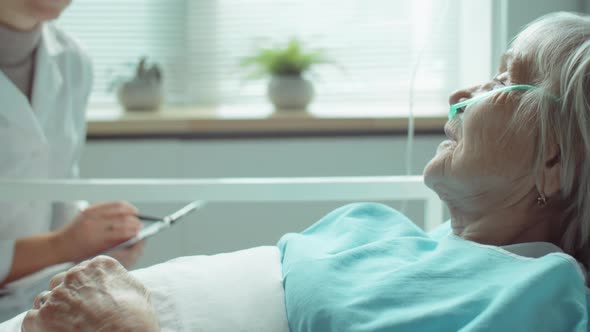 Senior Woman Lying on Hospital Bed and Talking with Female Doctor