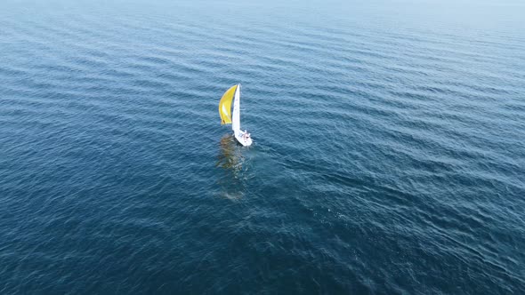 A small sailing ship with yellow and white sails sails on the blue sea.