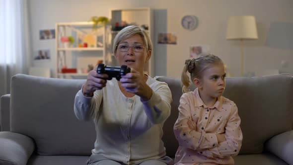 Excited Granny Playing Video Game Ignoring Sad Grandchild Sitting Sofa Addiction