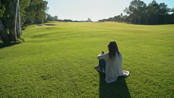 Shot of Girl Using Smartphone Sitting on a Grassy Field on a Sunny Day