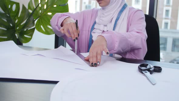 Small Business and Hobby Concept. Muslim Woman Fashion Designer Pinning Paper Pattern at the Table