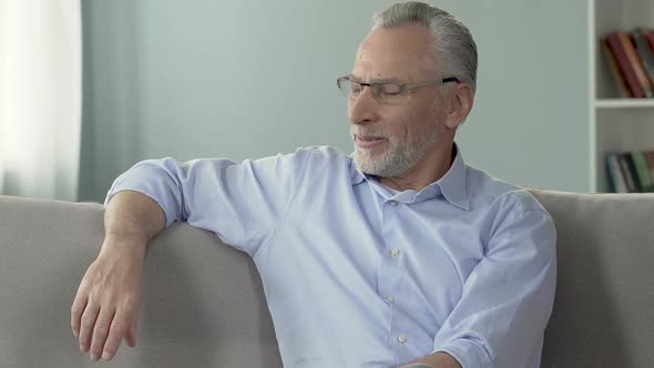 Senior man on couch looking aside and smiling, life experience and wisdom