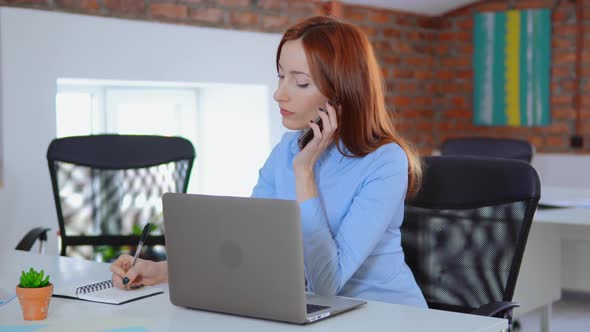 Business Woman with Cell Phone, Laptop Computer at Work in Office