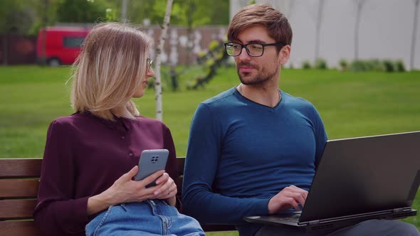 Two professional coworkers sitting on bench spring background.