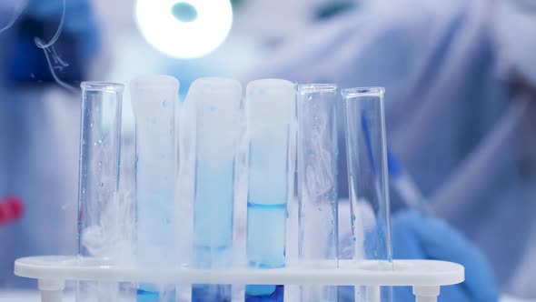 Close Up of Scientist Adding Solution with Pipette on Smoking Blue Fluid in Test Tubes