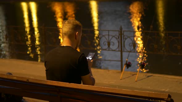 a Fisherman in a Black Tshirt Sits on a Bench and Talks on the Phone