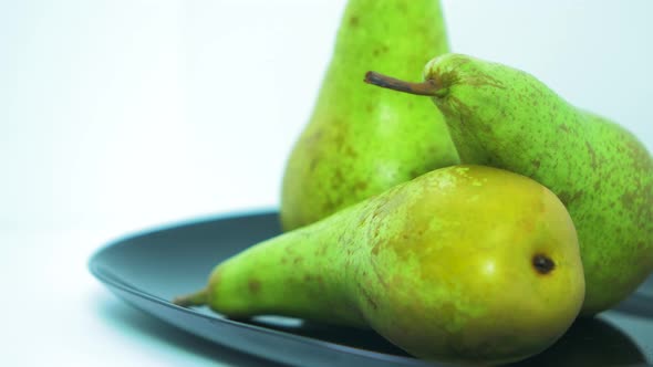 Fresh big green pears rotates slowly on a black plate on light blue background, healthy food concept