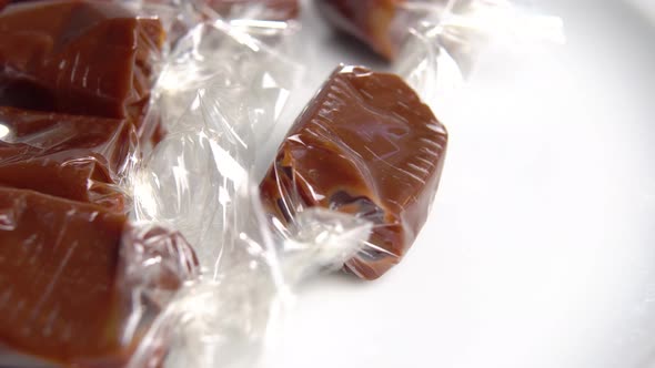 Brown cream caramel toffee candies in wrappers on a white plate. Macro