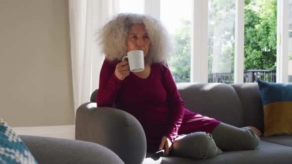 Senior caucasian woman drinking coffee while watching tv at home