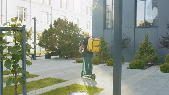 A Delivery Man with a Yellow Backpack Drives a Emoped Into the Video Frame Stops