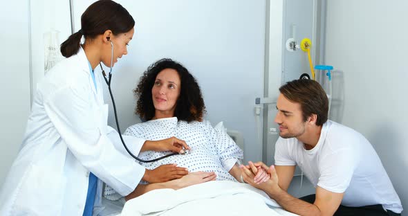 Doctor examining pregnant woman with stethoscope in ward