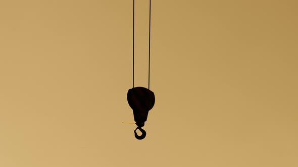 Silhouette of a Crane Hook Dangling in the Wind on a Construction Site