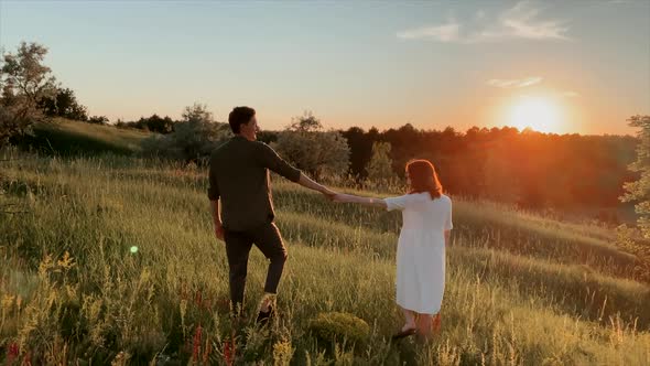 Romantic couple walking on the field in the evening sunset